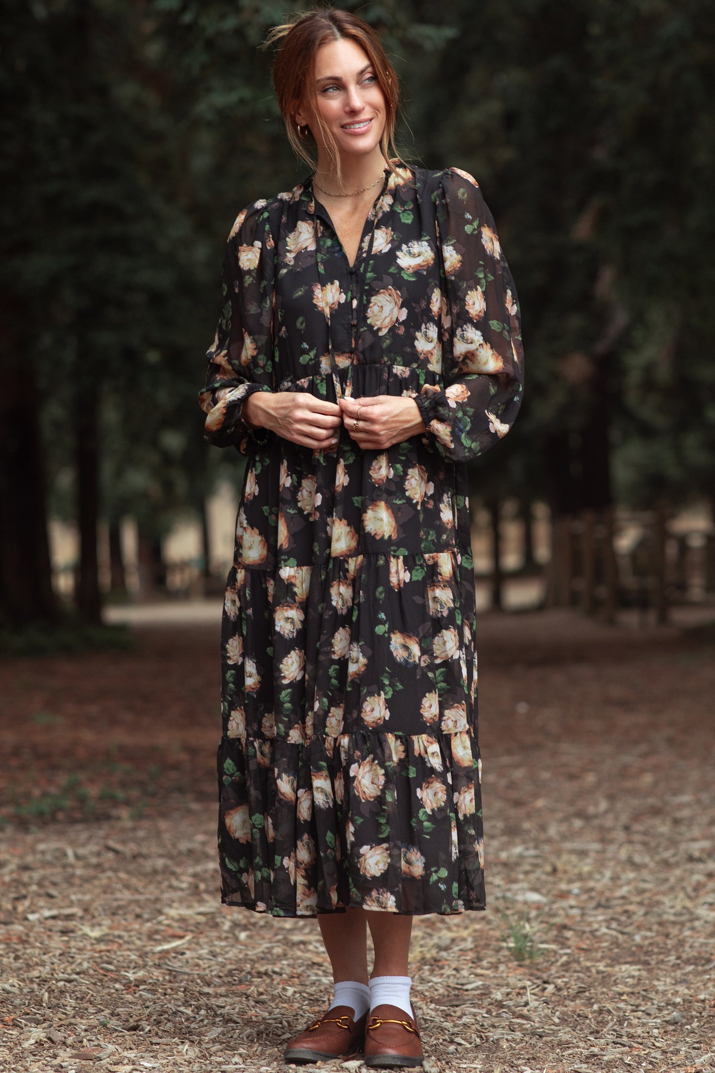 woman wearing a black floral long sleeve maxi dress with a tiered skirt and puff sleeves in a forest setting
