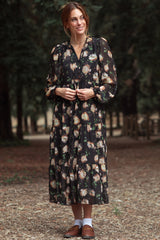 woman wearing a black floral long sleeve maxi dress with a tiered skirt and puff sleeves in a forest setting