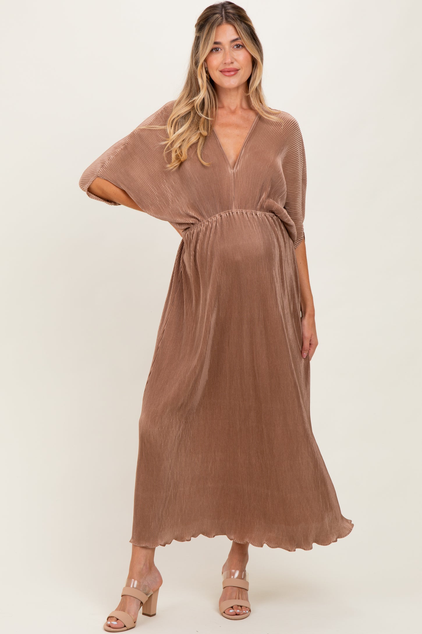 woman wearing a brown pleated maternity dress with a v-neck and cinched waist, showcasing her baby bump