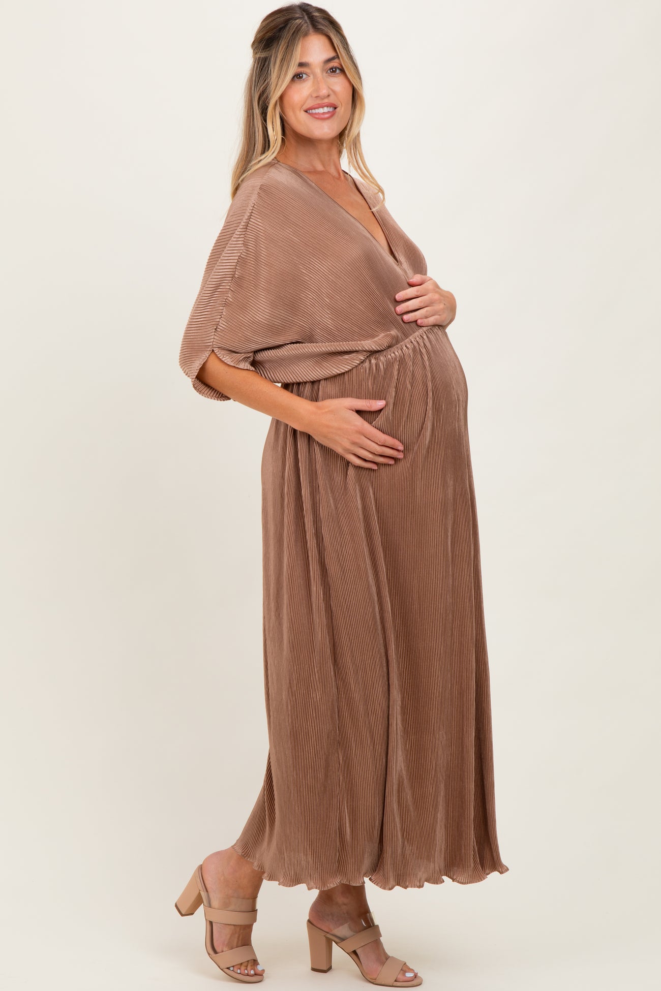 woman wearing a brown pleated maternity maxi dress and holding her baby bump
