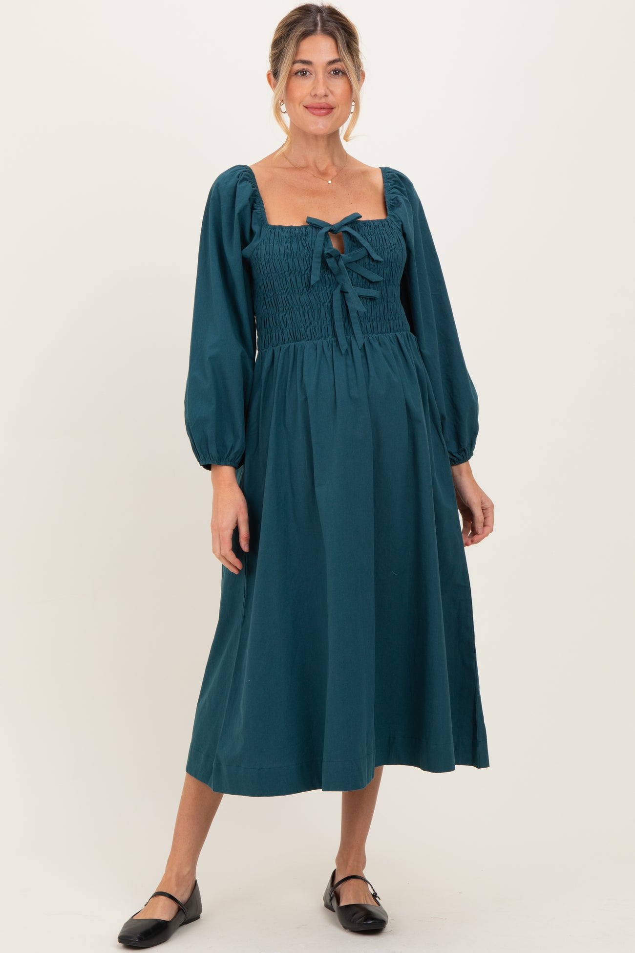woman wearing a teal maternity midi dress with puff sleeves and a smocked bodice, holding her baby bump