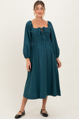 woman wearing a teal maternity midi dress with puff sleeves and a smocked bodice, holding her baby bump