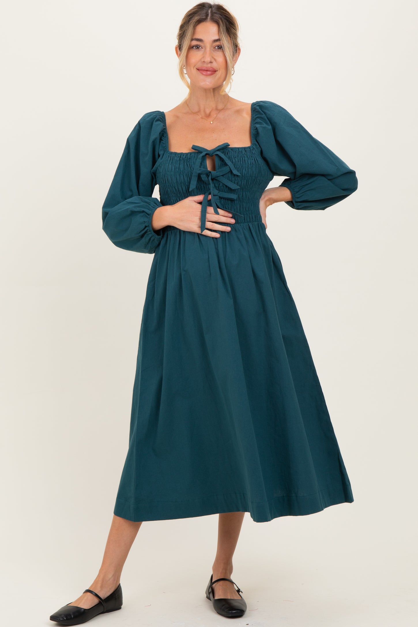 woman wearing a teal maternity dress with puff sleeves and smocked bodice, holding her baby bump