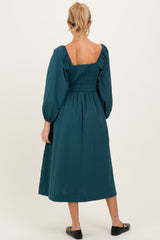 woman wearing a teal maternity midi dress with puff sleeves and a smocked bodice, showing her back