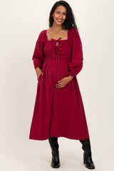 woman wearing a burgundy maternity dress with puff sleeves and a smocked bodice, holding her baby bump