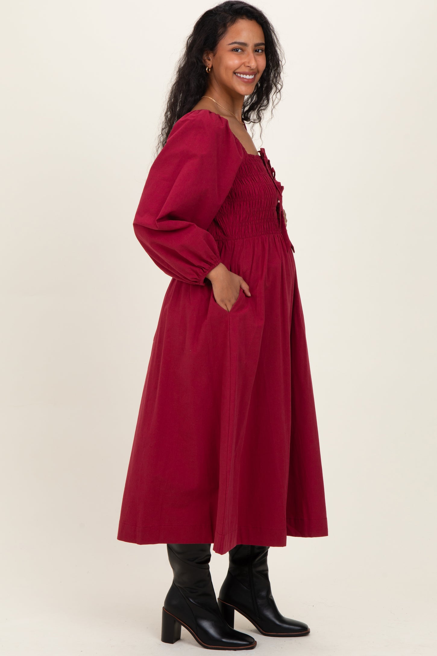 woman wearing a burgundy maternity dress with puff sleeves and pockets, showcasing her baby bump