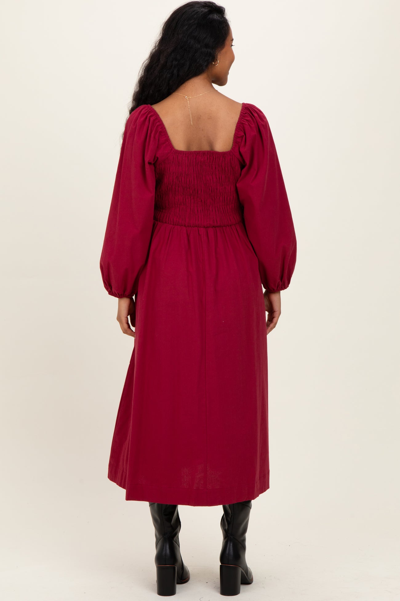 woman wearing a burgundy maternity dress with puff sleeves and a smocked bodice, showing her back