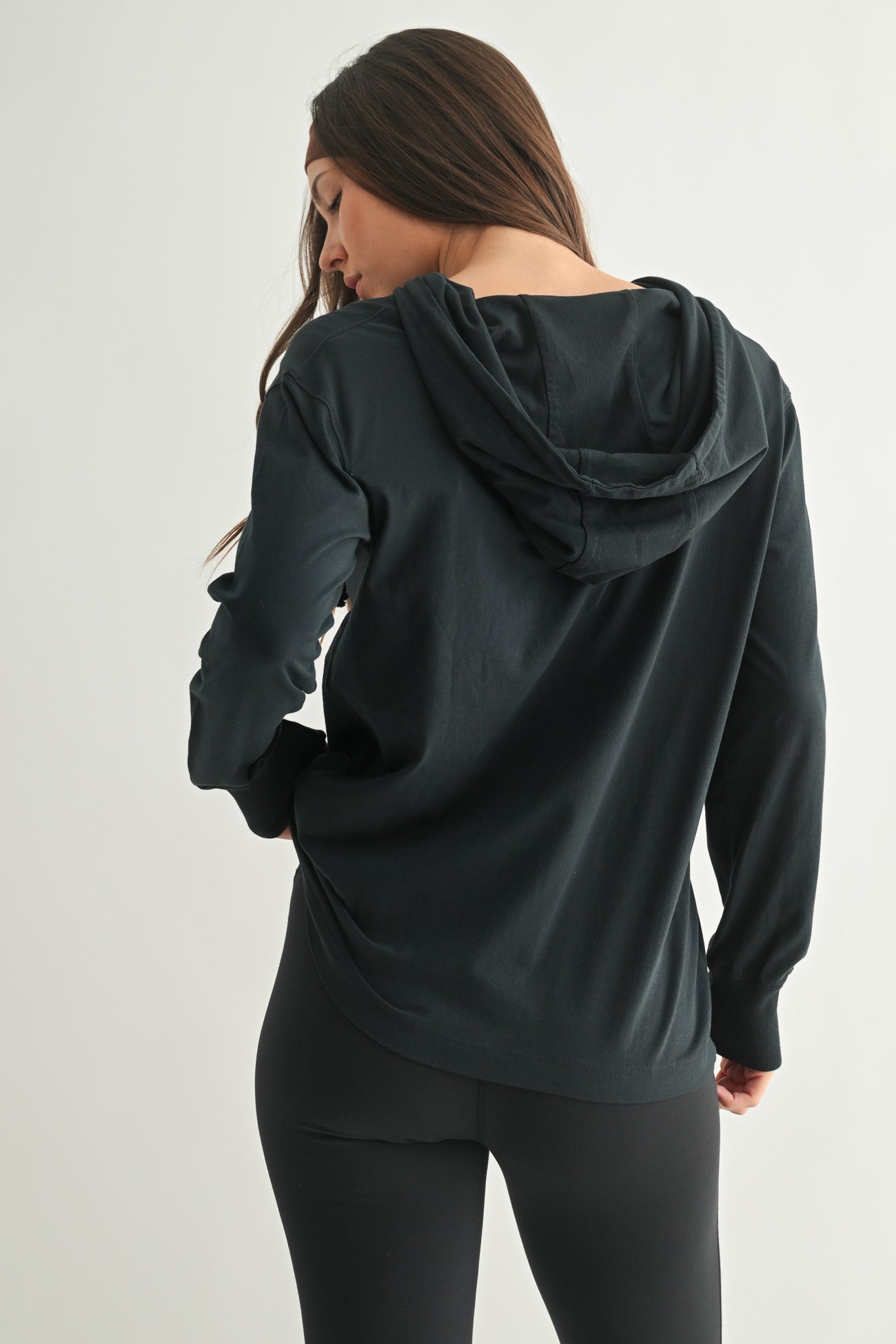 woman wearing a black long sleeve hoodie, shown from the back, paired with black leggings