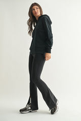 woman wearing a black hoodie and black flared leggings with side slits paired with sporty sneakers
