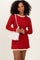 woman wearing a red ribbed long sleeve dress with ruffled cream trim, holding a white handbag