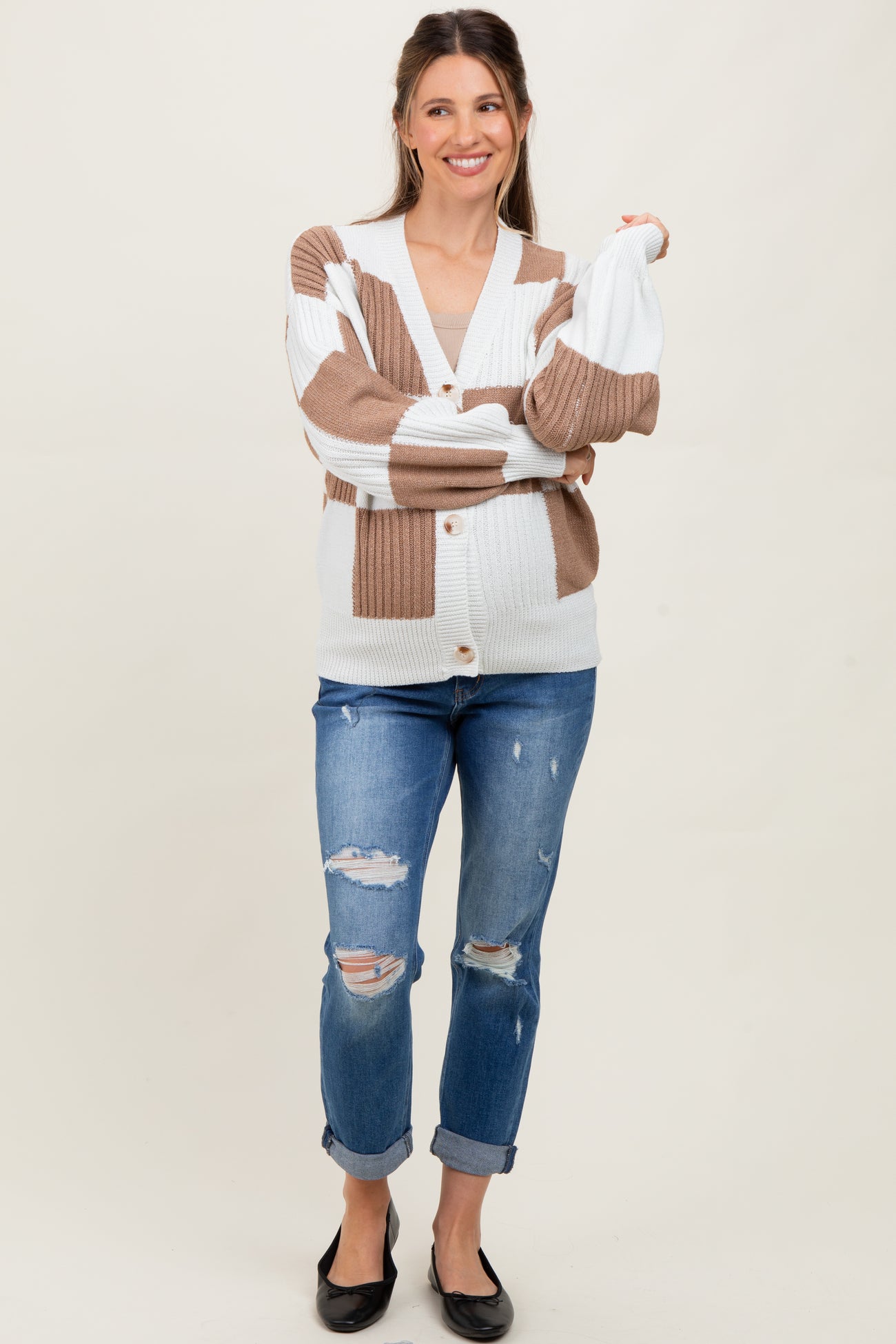 woman wearing a striped brown and white maternity sweater with buttons, paired with distressed blue jeans