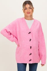 woman wearing a pink maternity cardigan with a v-neck and button details, showing her baby bump