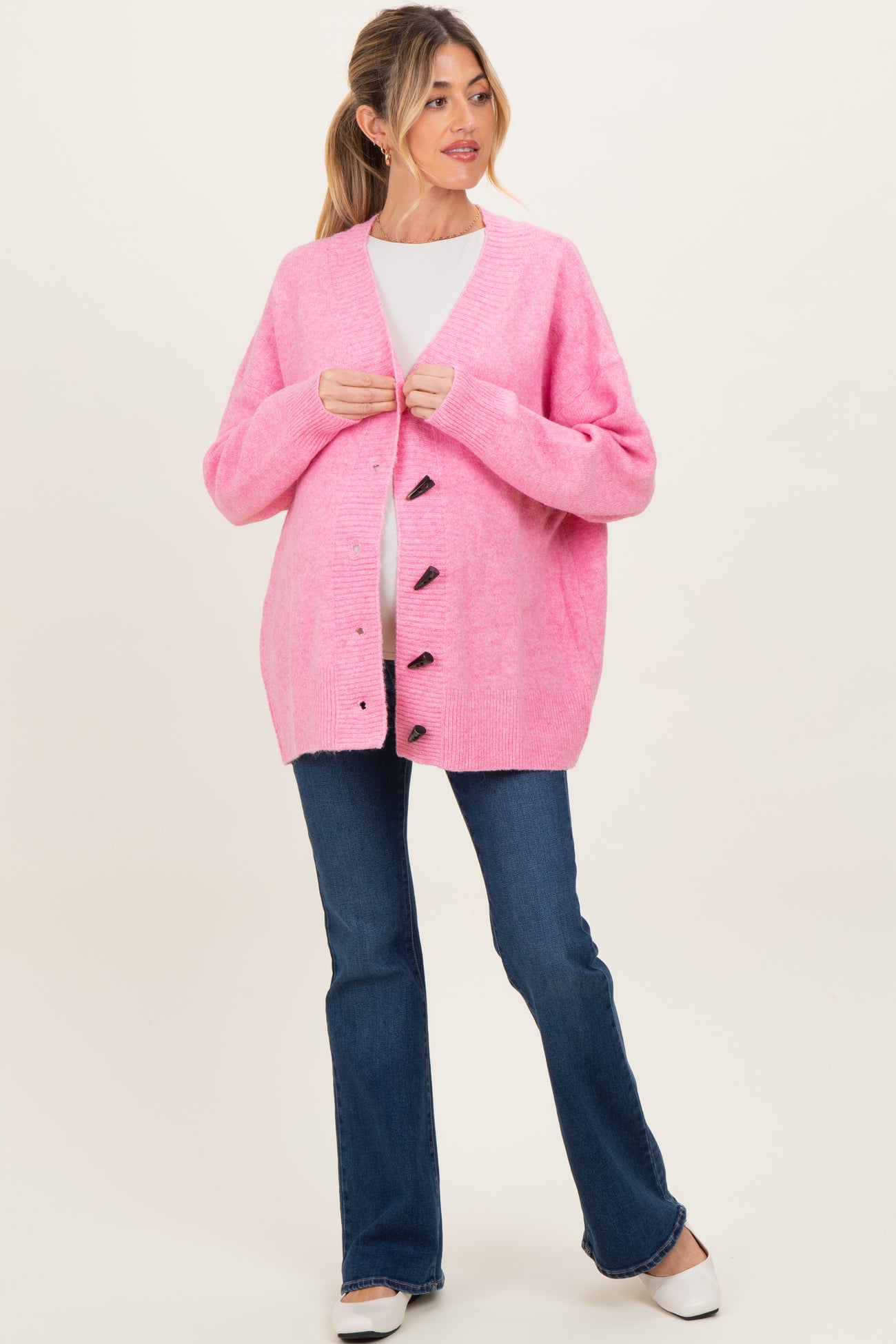 woman wearing a bright pink maternity cardigan over a white top, with a visible baby bump and blue flared jeans