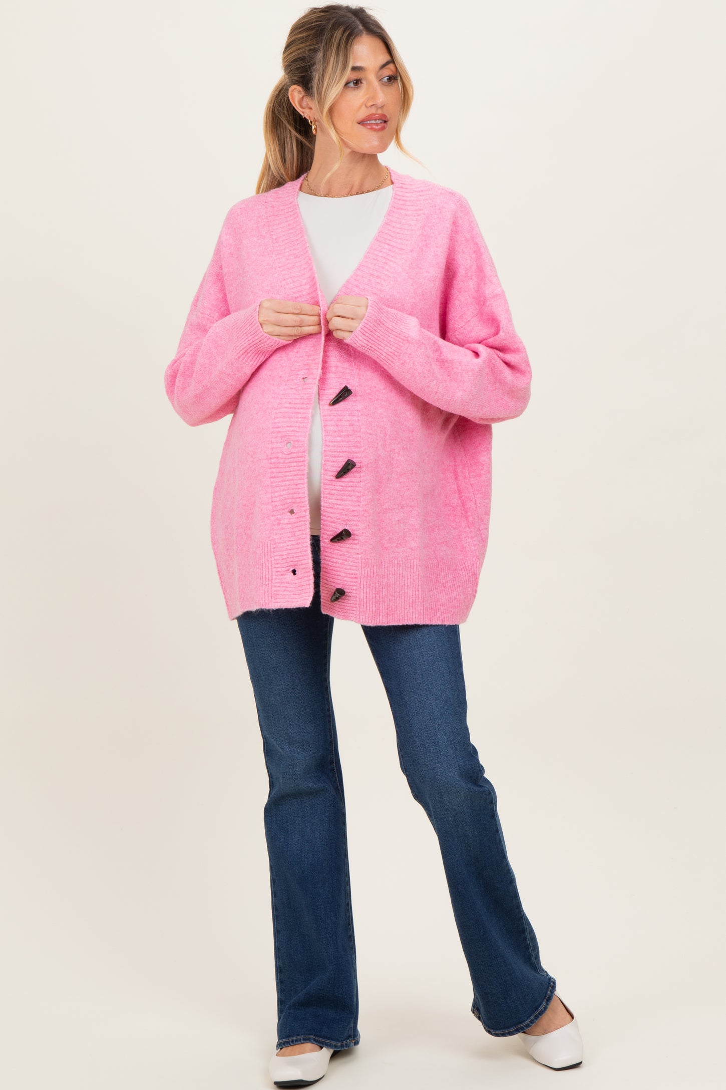 woman wearing a bright pink maternity cardigan over a white top, with a visible baby bump and blue flared jeans