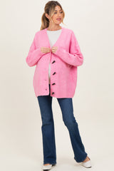 woman wearing a bright pink maternity cardigan over a white top, with a visible baby bump and blue flared jeans