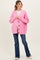 woman wearing a bright pink maternity cardigan over a white top, with a visible baby bump and blue flared jeans