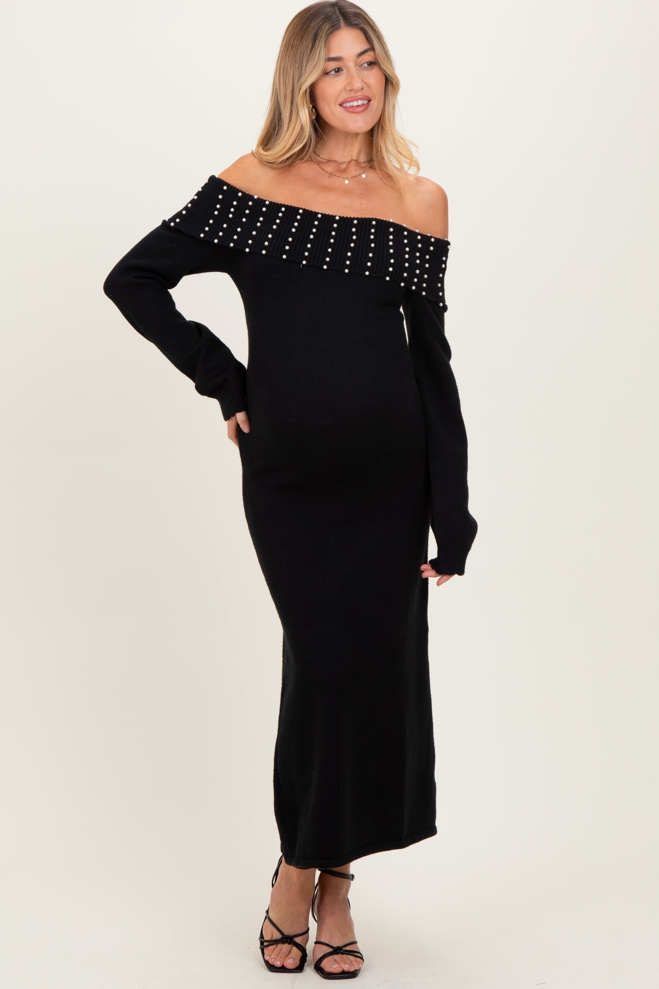 woman wearing a black off-the-shoulder maternity dress with studded details and a visible baby bump
