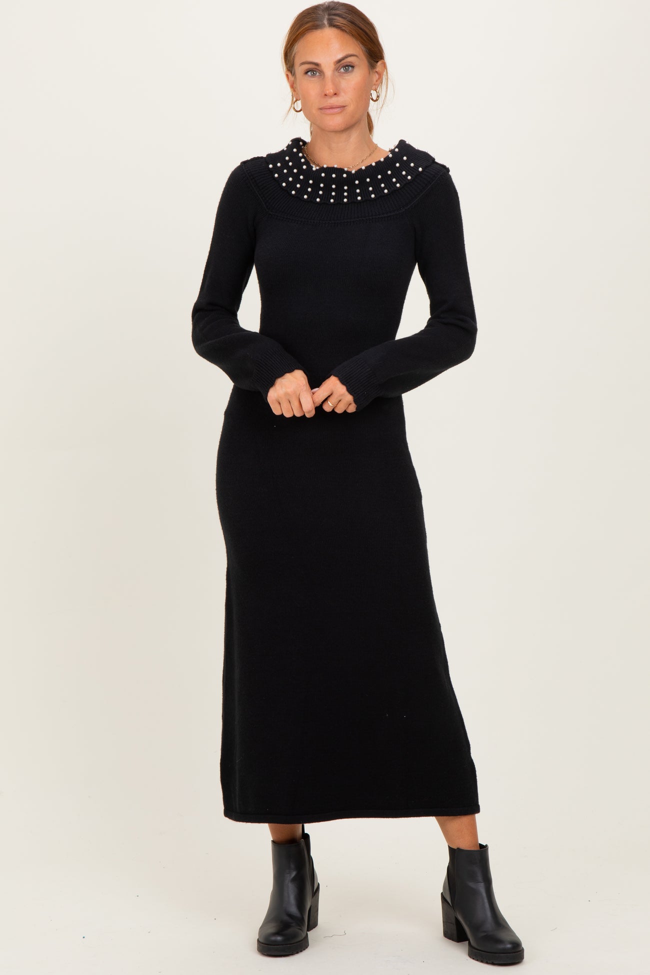 woman wearing a black long sleeve sweater dress with a decorative pearl collar and ankle boots
