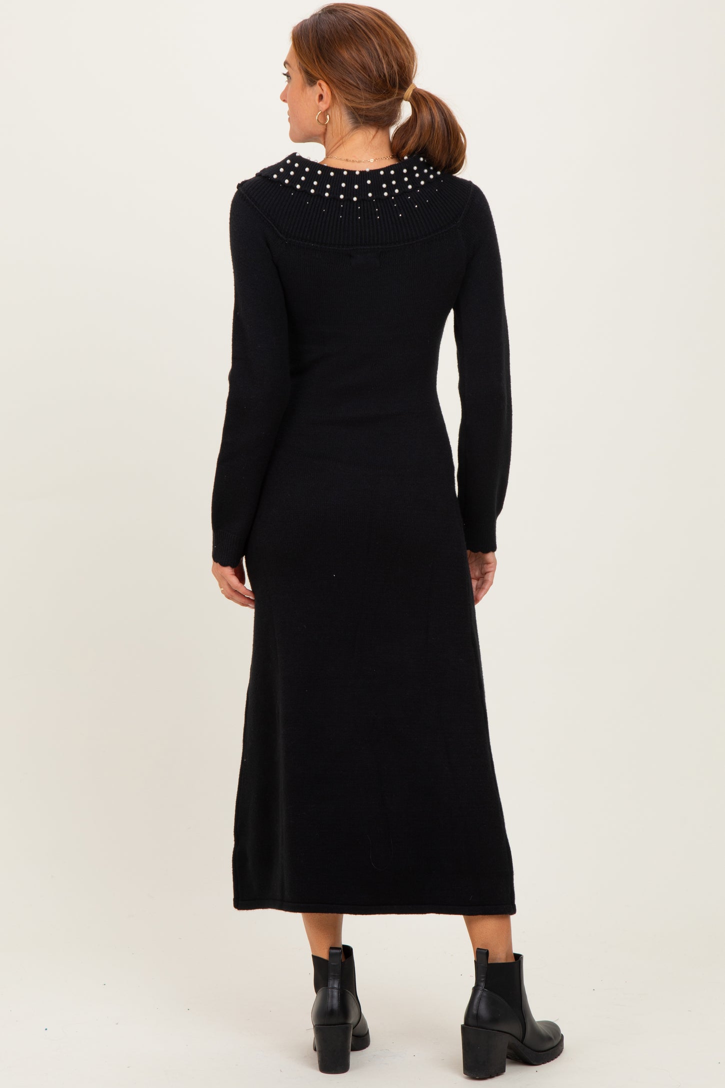 woman wearing a black long sleeve knitted dress with a studded collar and ankle boots, shown from the back