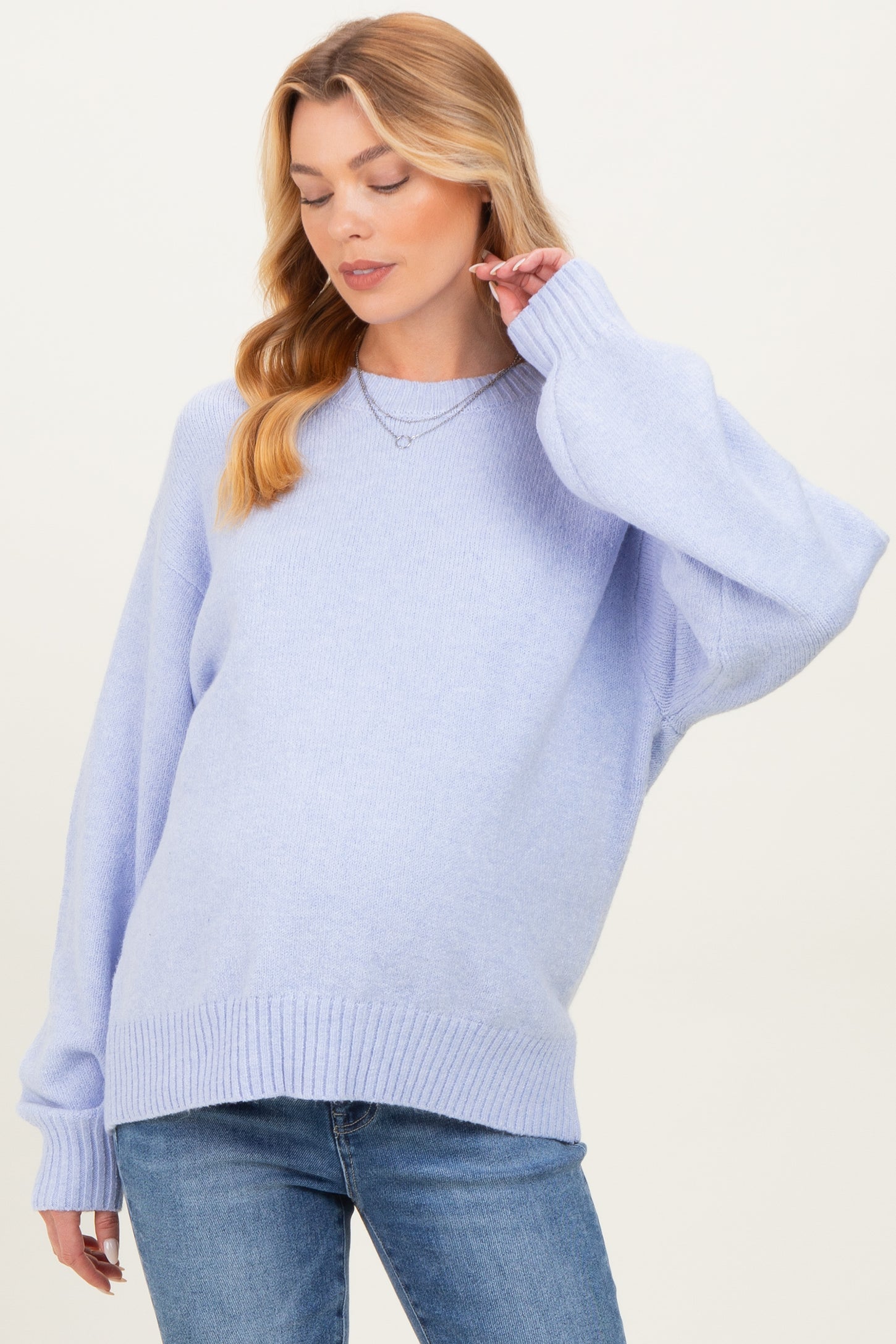 woman wearing a light purple oversized maternity sweater with long sleeves and ribbed hem, posing gently with her hand on her neck