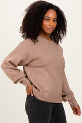 woman wearing a taupe oversized sweater with ribbed hem and cuffs, standing against a plain background