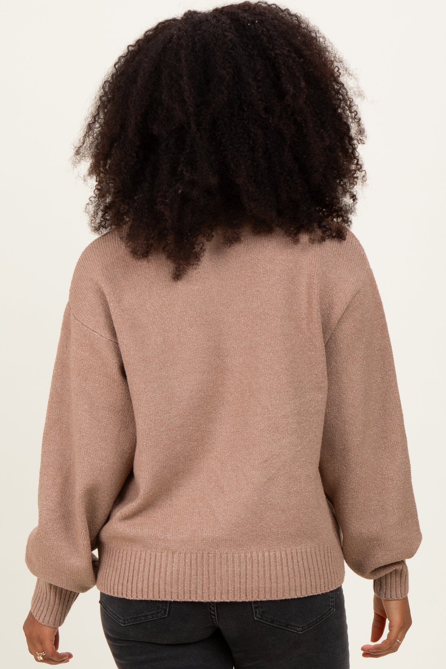 woman wearing a beige oversized sweater with balloon sleeves and a ribbed hem, viewed from the back