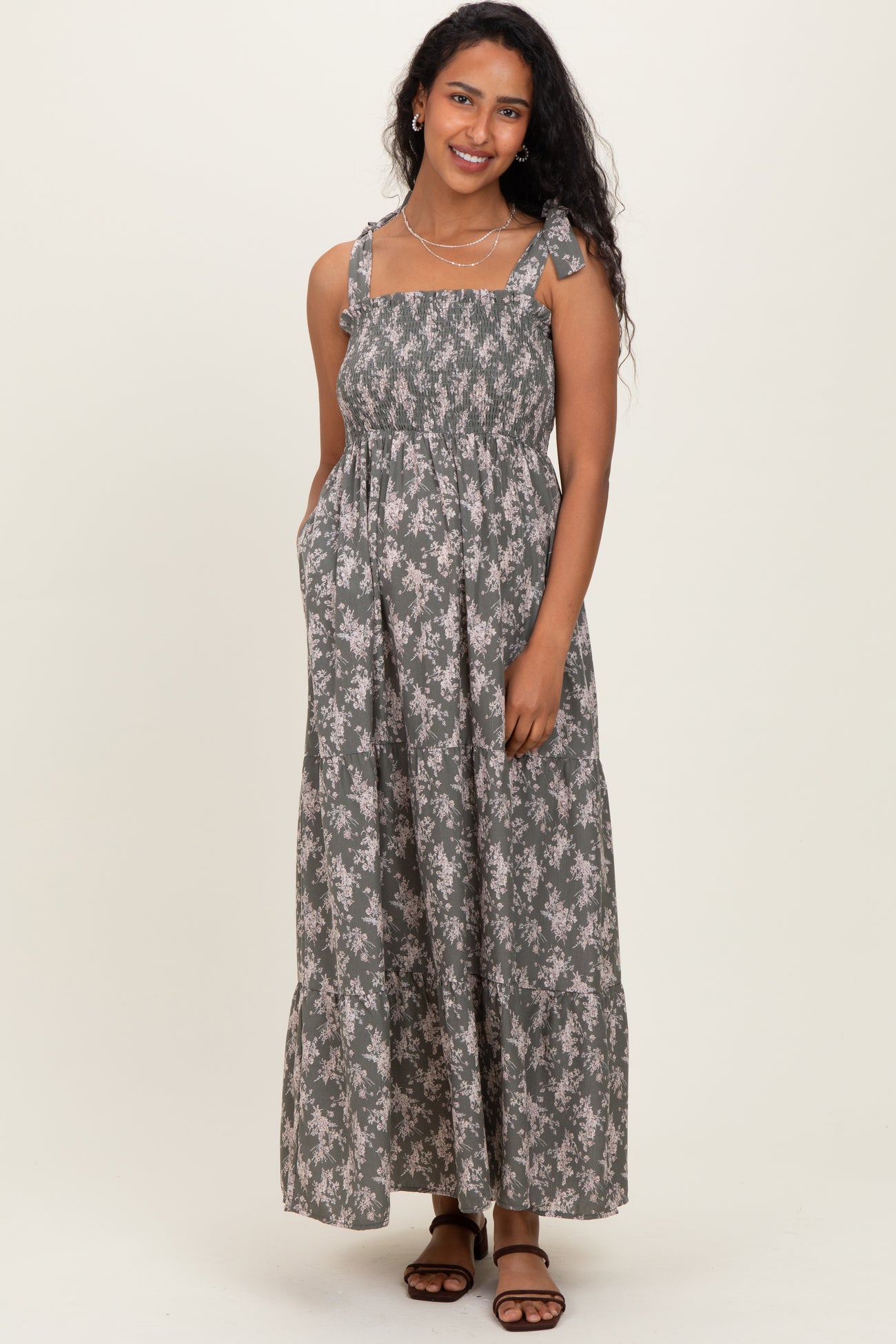 woman wearing a floral patterned gray maternity maxi dress with adjustable straps and pockets
