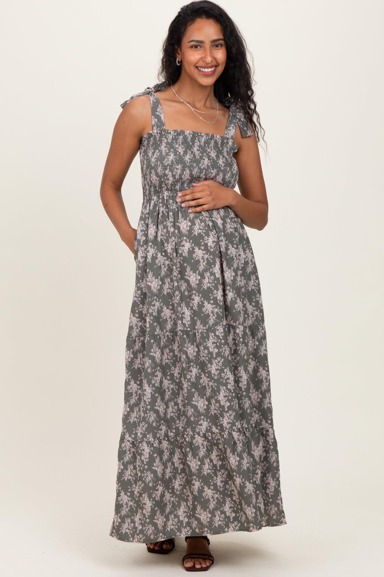 woman wearing a floral print maternity maxi dress with adjustable straps, holding her baby bump