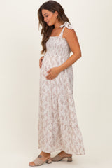 woman wearing a light pink floral maternity maxi dress with tie straps and holding her baby bump