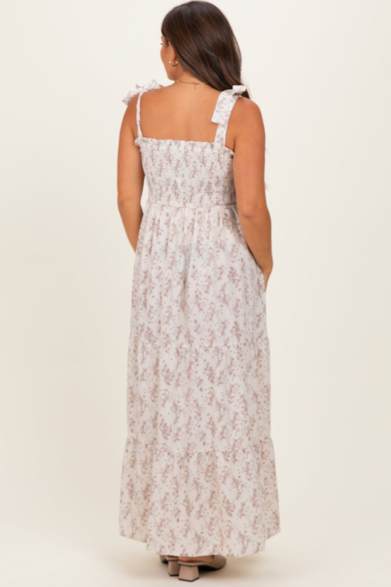 woman wearing a back view of a floral print maternity maxi dress with tie straps and a smocked bodice