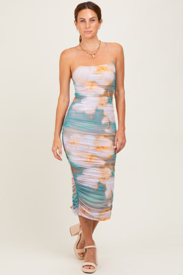 woman wearing a fitted midi dress with a turquoise and orange floral print and side ruching, standing on a neutral background