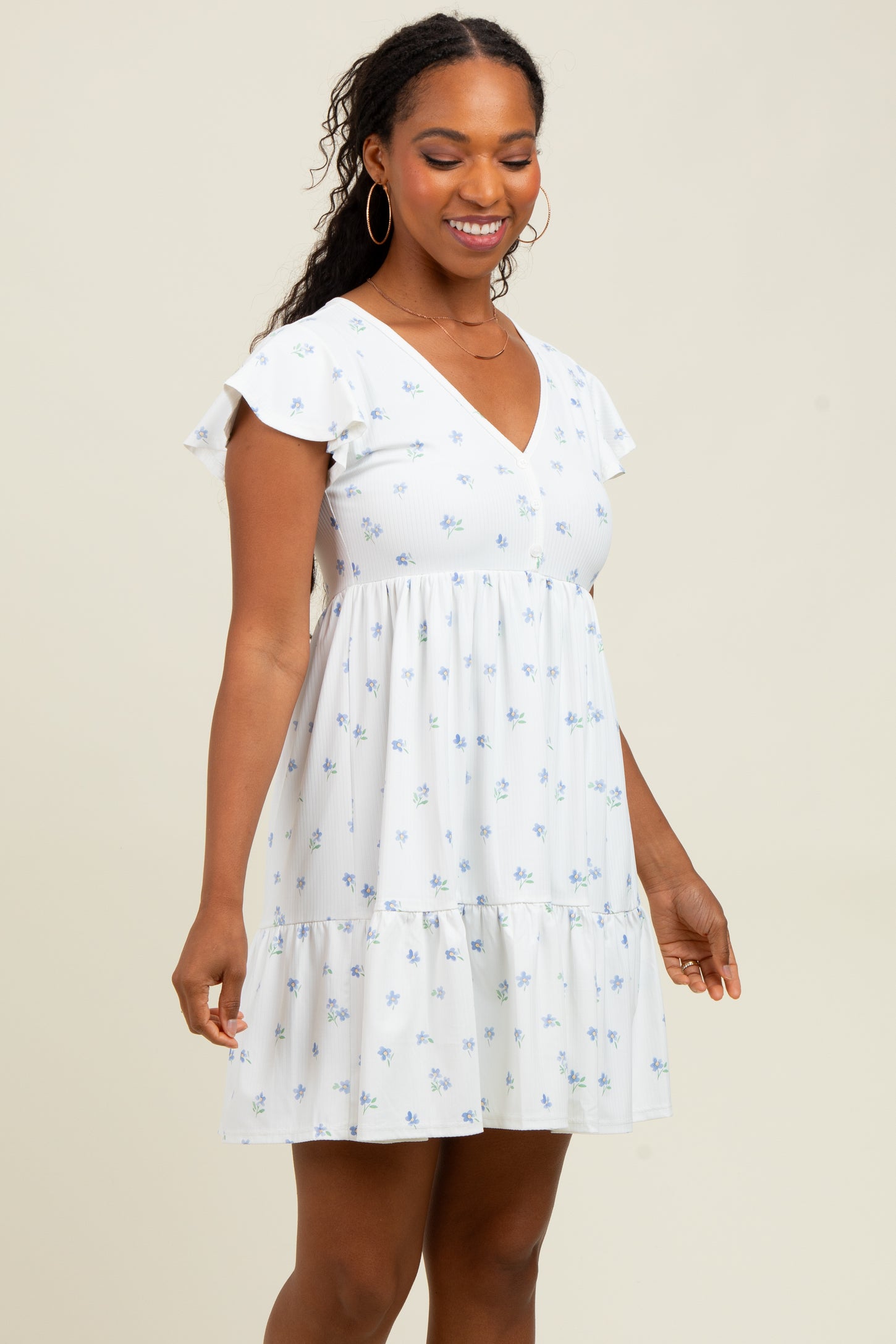 woman wearing a white floral mini dress with flutter sleeves and a tiered hem, smiling at the camera