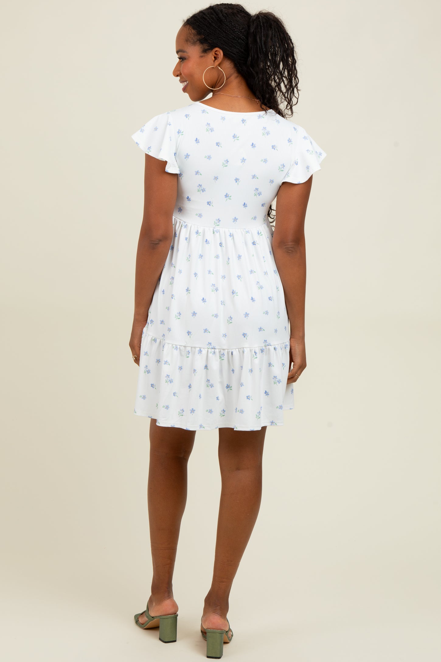 woman wearing a white floral short sleeve dress with ruffle details and a tiered skirt, viewed from the back