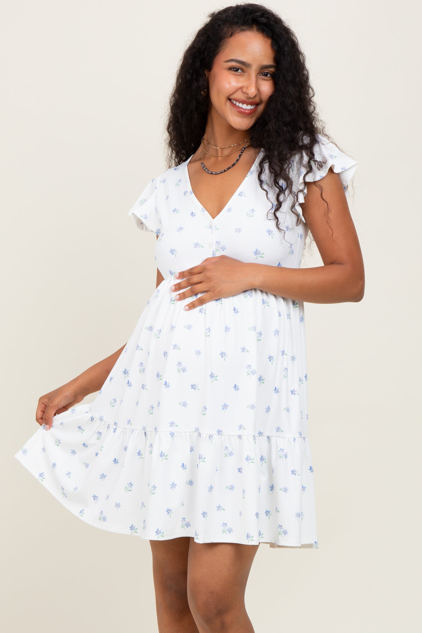 woman wearing a white floral maternity dress with ruffle sleeves and a tiered skirt, holding her baby bump