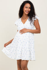 woman wearing a white floral maternity dress with ruffle sleeves and a tiered skirt, holding her baby bump