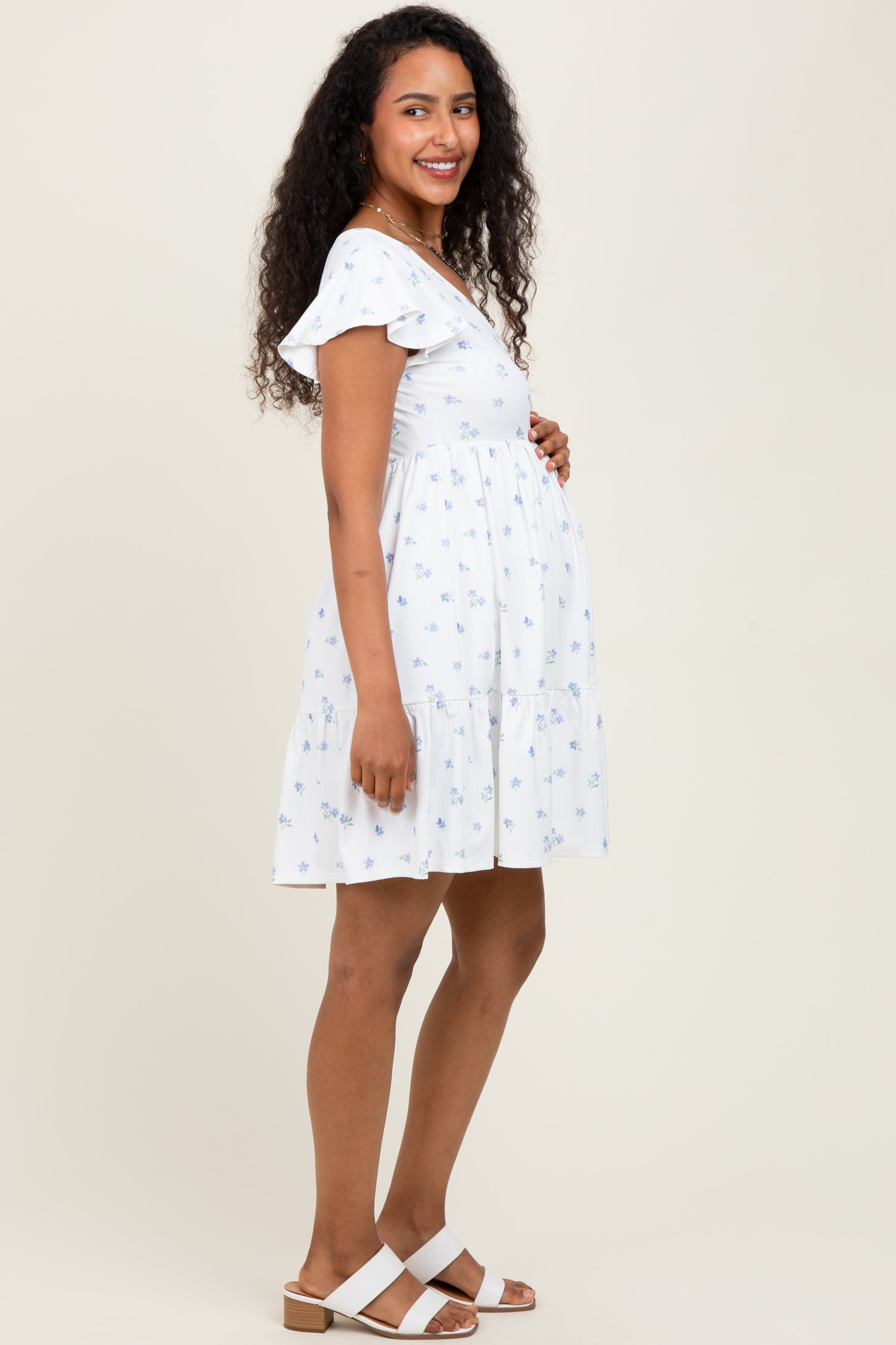 woman wearing a white floral maternity dress with ruffle sleeves and a visible baby bump