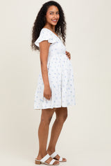 woman wearing a white floral maternity dress with ruffle sleeves and a visible baby bump