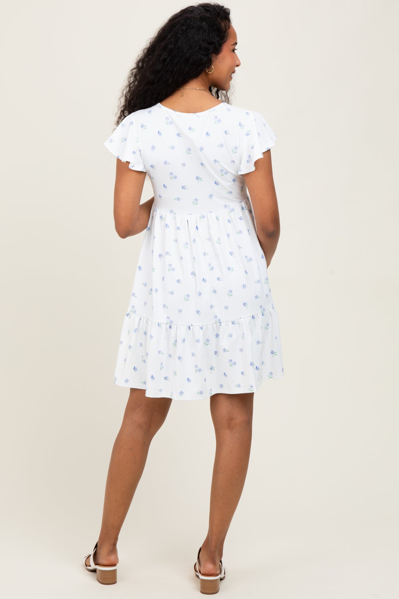 woman wearing a white maternity dress with blue floral print and ruffled sleeves, showing a baby bump from behind