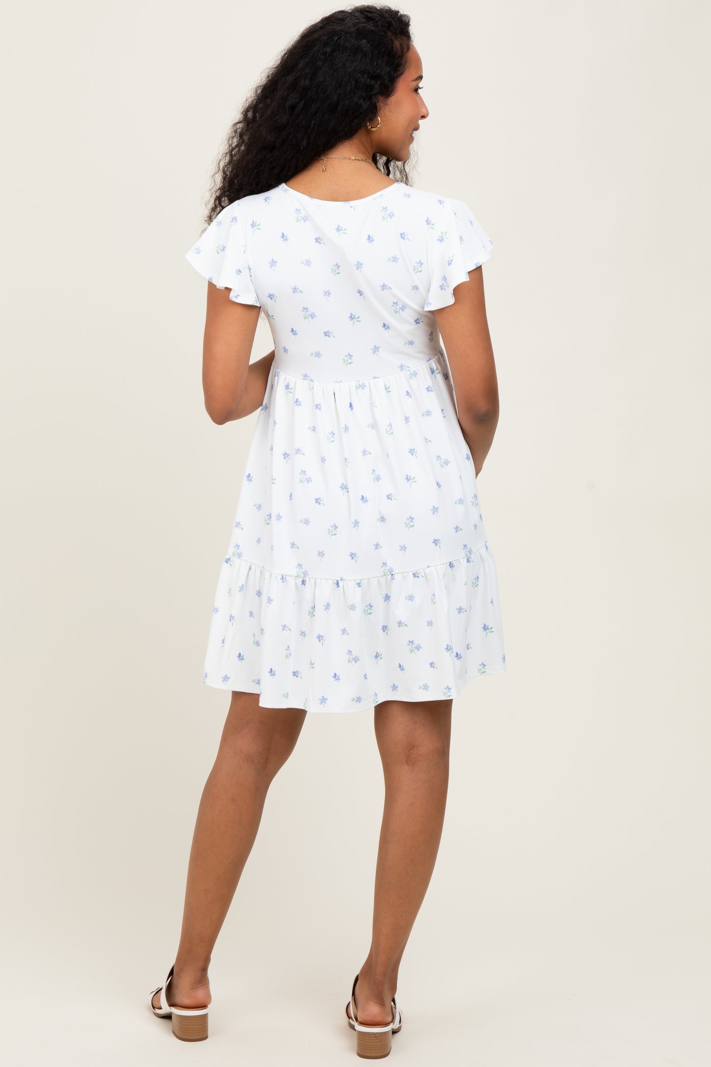 woman wearing a white maternity dress with blue floral print and ruffled sleeves, showing a baby bump from behind