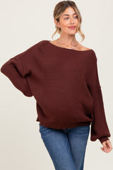 woman wearing a dark brown oversized knit maternity sweater and fitted jeans, with a relaxed fit and boat neckline