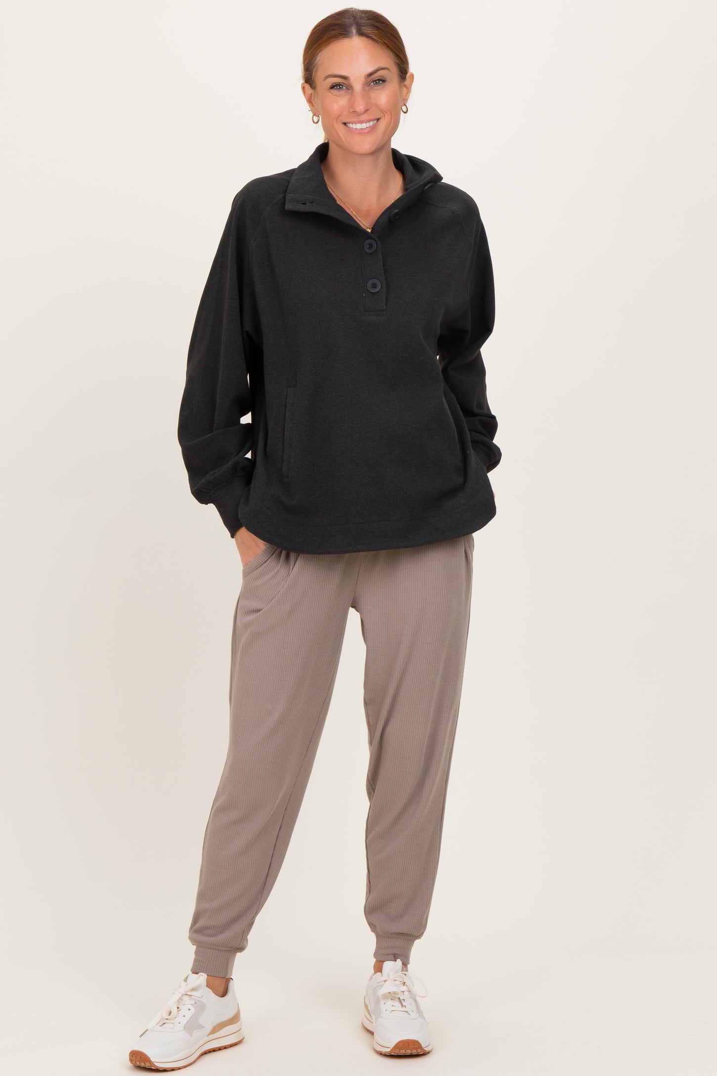 woman wearing a black fleece pullover with a collar and buttons paired with relaxed beige joggers and white sneakers