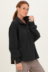 woman wearing a black pullover fleece top with buttons and a collar, styled with long sleeves and a relaxed fit