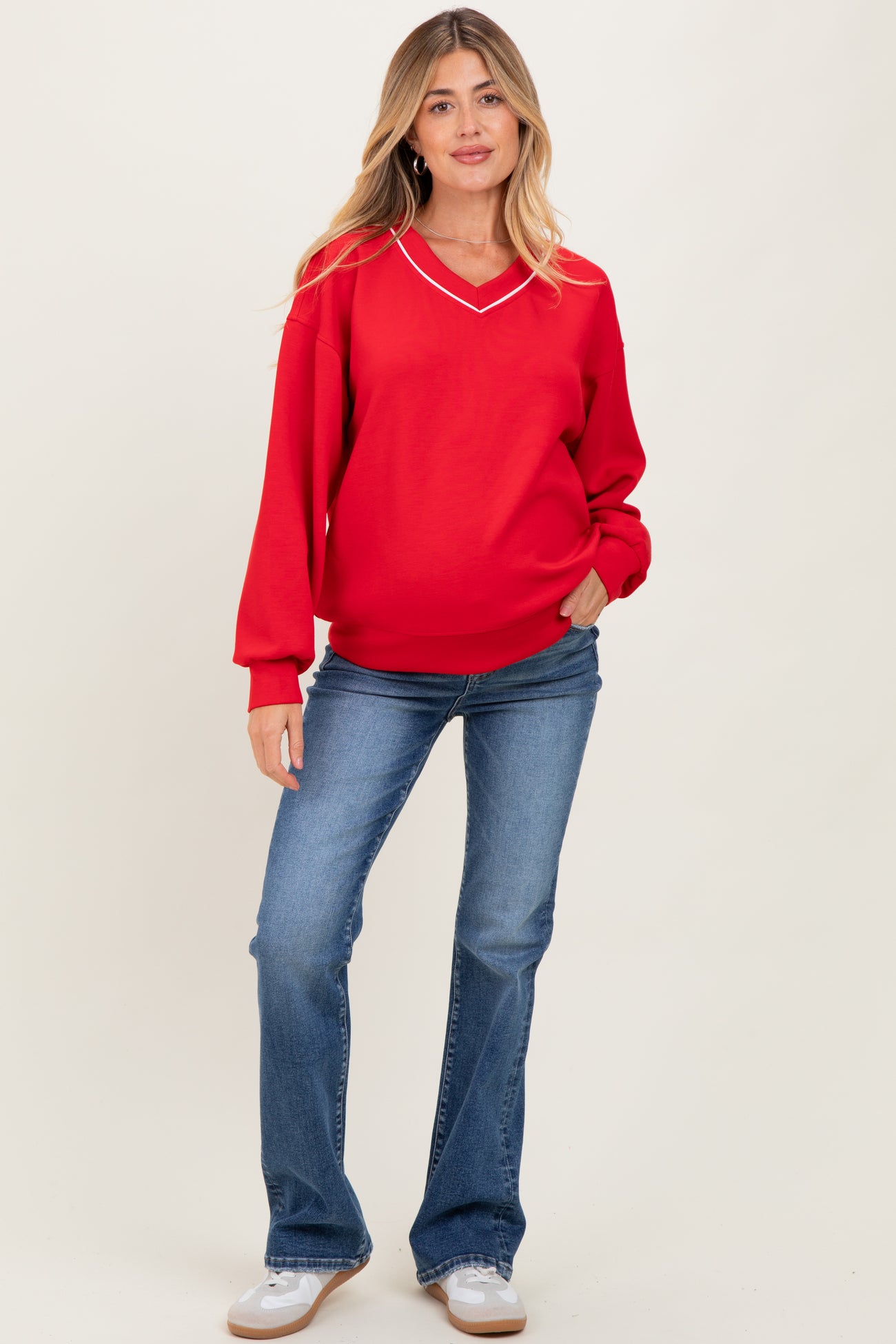 woman wearing a red maternity sweatshirt with a v-neckline and white piping, paired with blue flared jeans
