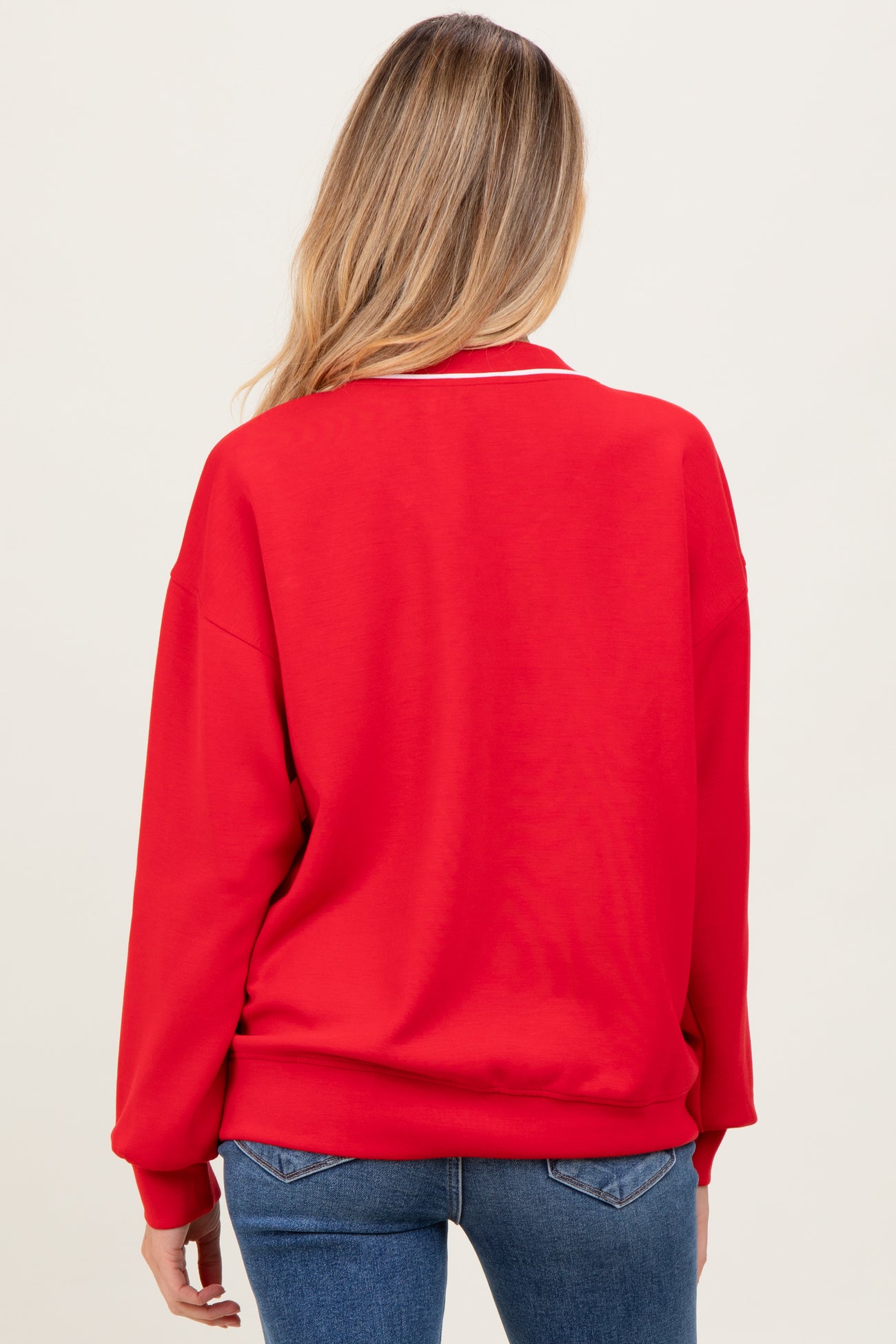 woman wearing a red maternity sweatshirt with a relaxed fit and white neckline details, showing a baby bump from the back