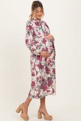 woman wearing a floral maternity dress with long sleeves and a tie neck, cradling her baby bump