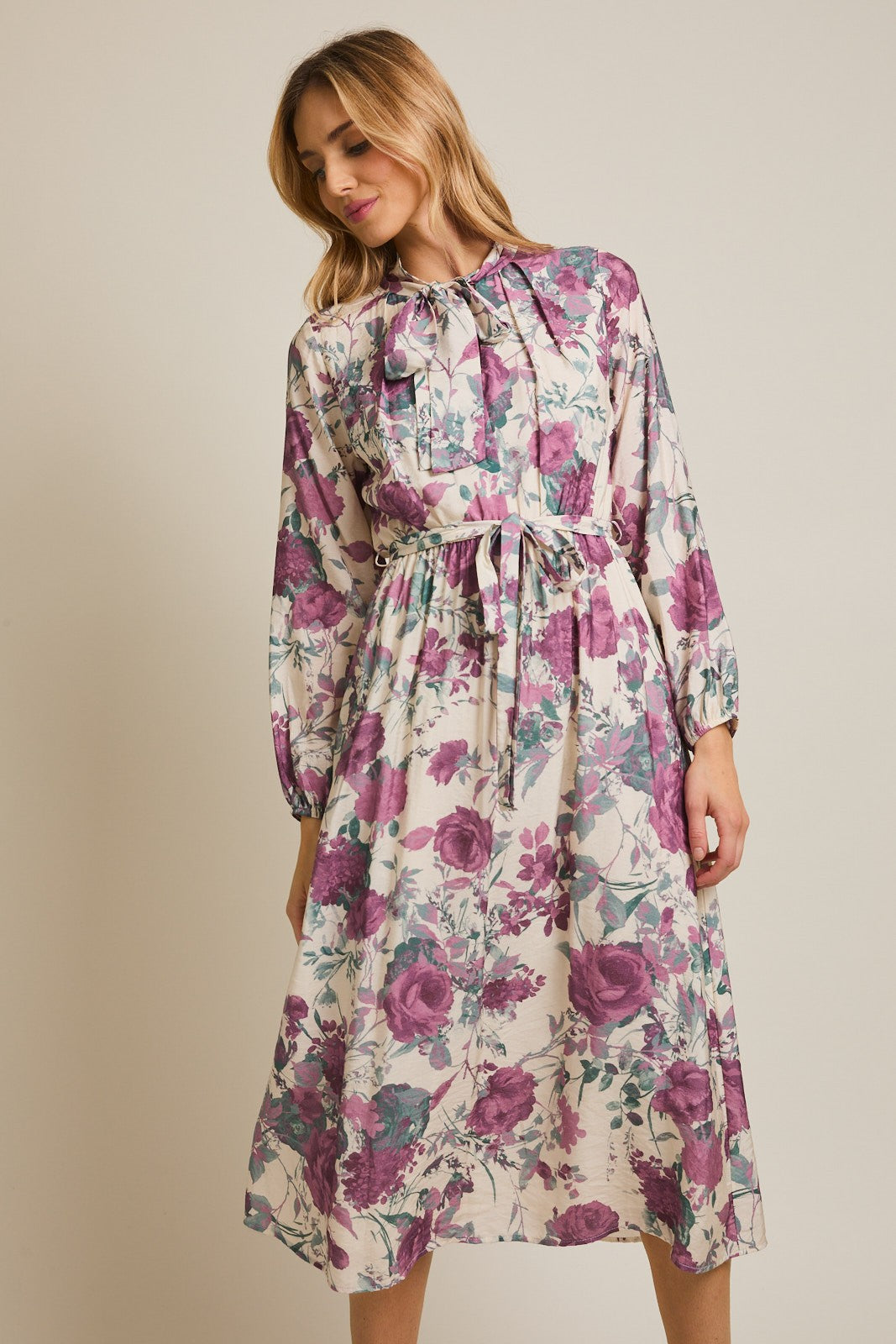 woman wearing a floral midi dress with purple and green hues, featuring a bow tie neckline and long sleeves