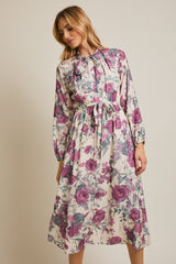woman wearing a floral midi dress with purple and green hues, featuring a bow tie neckline and long sleeves