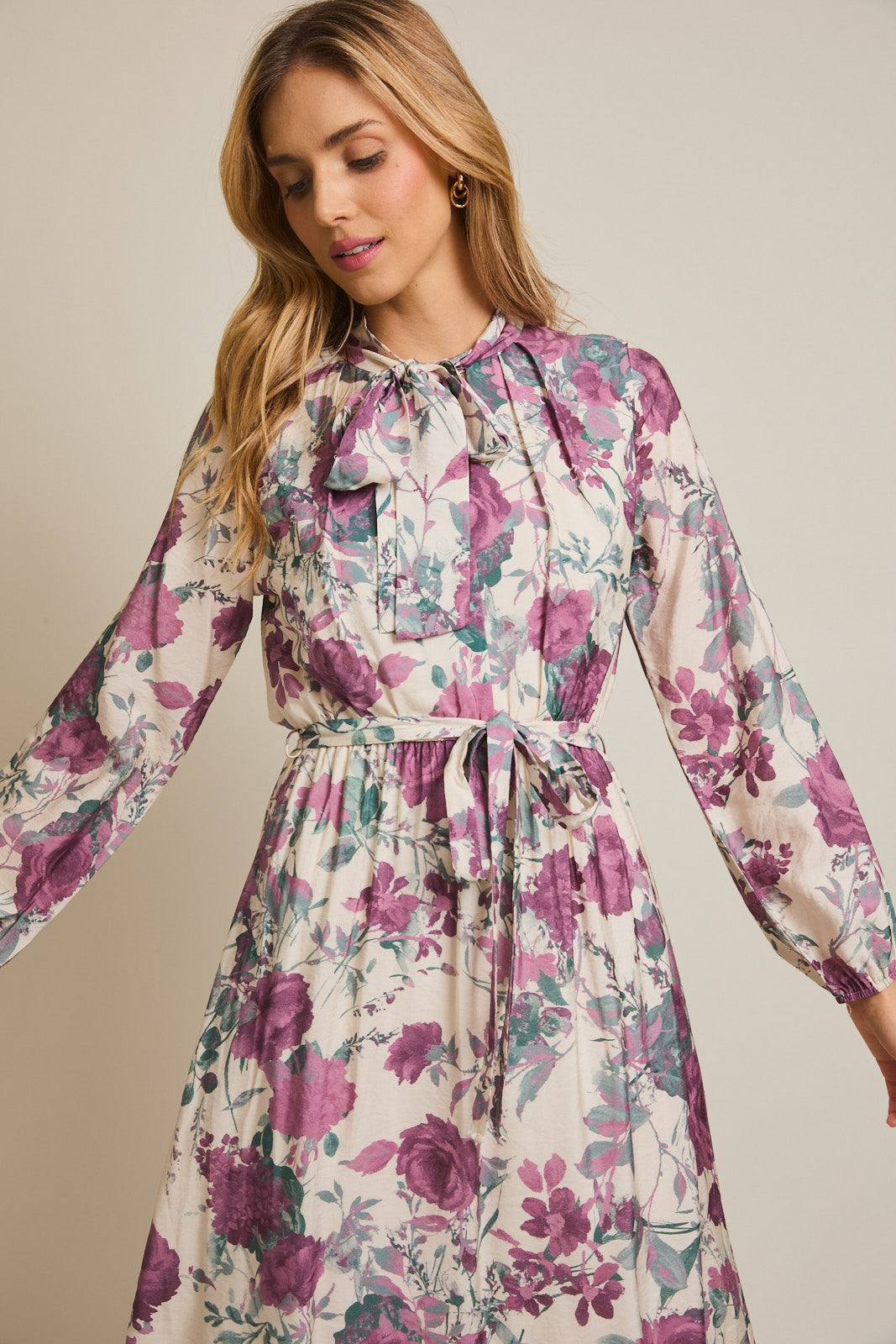 woman wearing a floral long sleeve dress with a bow tie neckline and a cinched waist