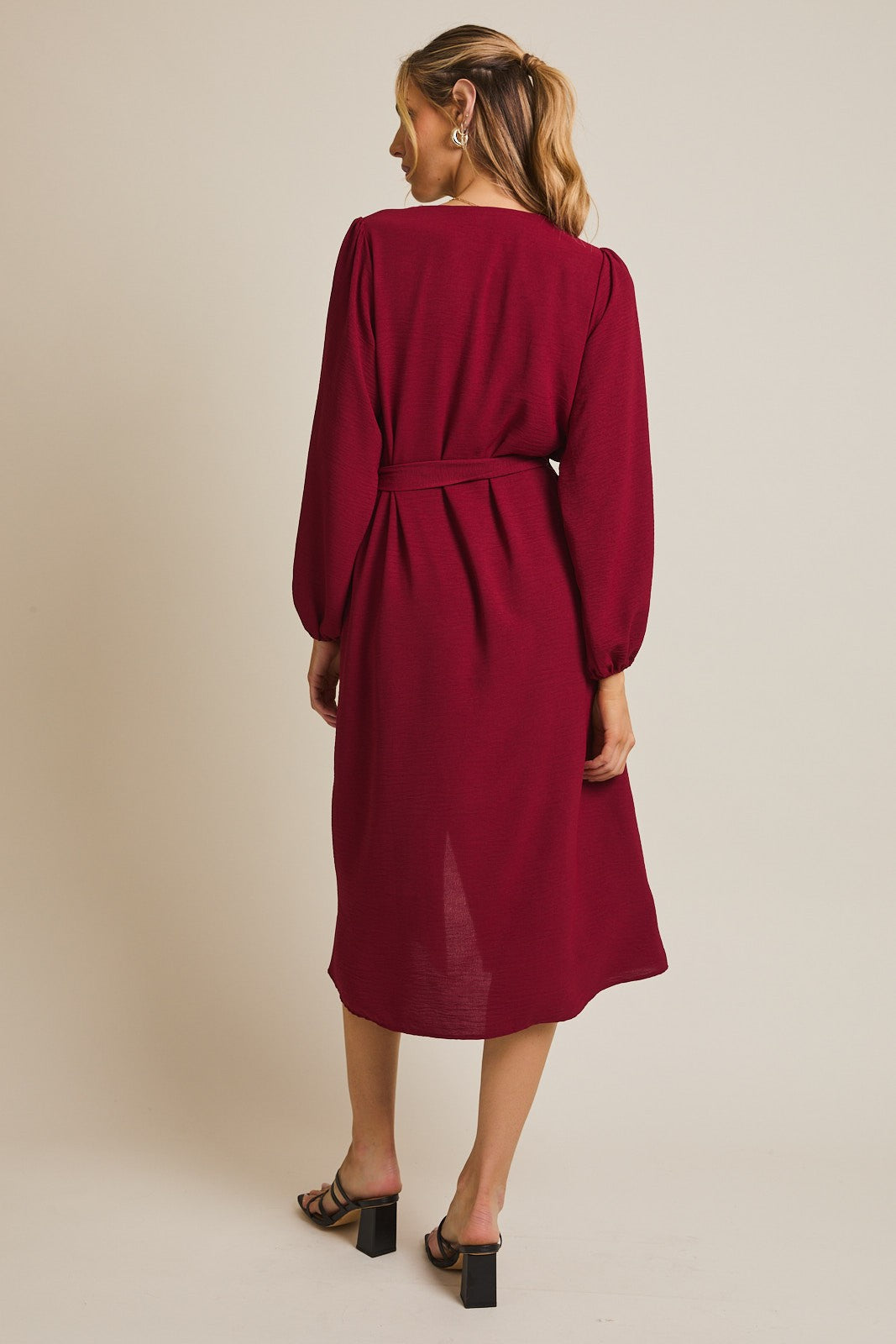 woman wearing a burgundy long sleeve dress with a tie belt and a midi length, showing the back view