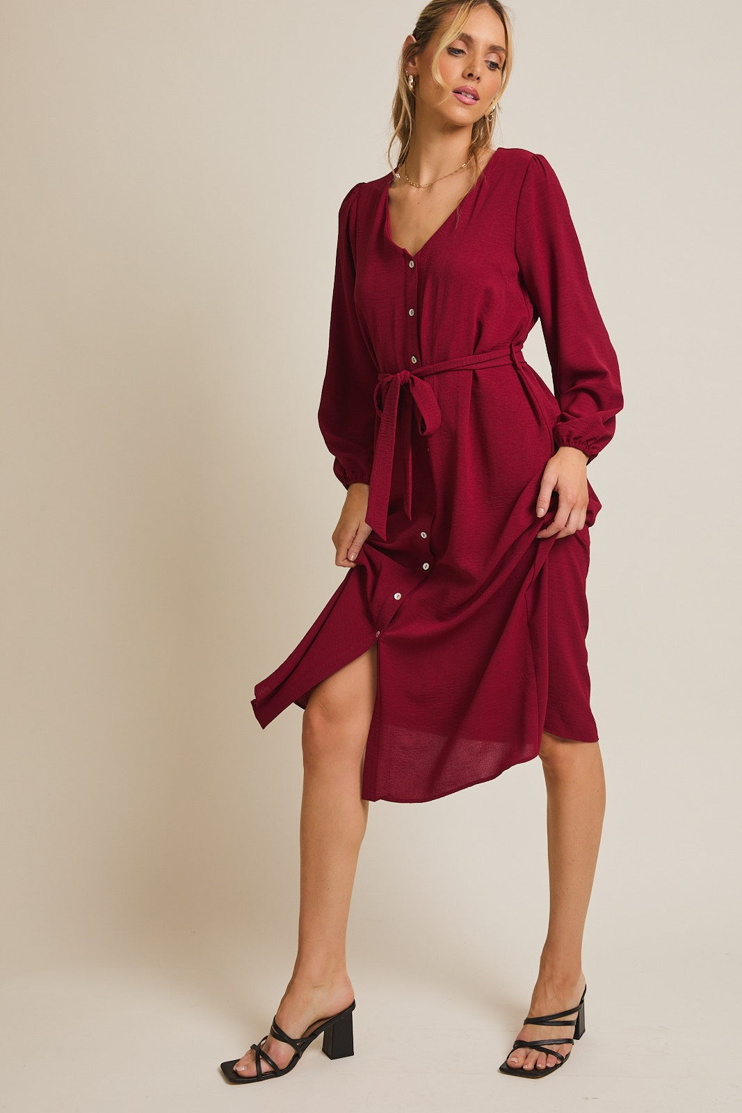 woman wearing a burgundy button-down midi dress with long sleeves and a tied waist, paired with black strappy heels